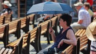 Hitze kann krank machen: Ein Frau sitzt unter einem Schirm auf einer Bank.