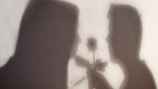 Die Schatten zweier Menschen stehen sich gegenüber - der rechte überreicht eine Rose.