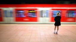 Junge Frau steht am Bahnsteig während ein Zug der Deutschen Bahn vorbeifährt. 