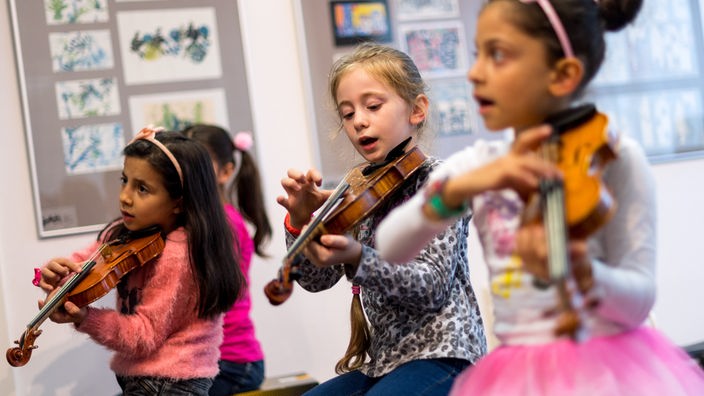 Drei Mädchen spielen Geige.