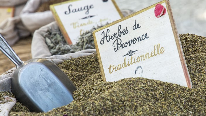 Ein Sack voller Kräuter, darin ein Schild mit der Aufschrift "Herbes de Provence traditionelle" und eine kleine Schaufel