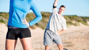 Junge Frau und junger Mann machen Dehnübungen am Strand. 