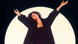 Die Sängerin und Schauspielerin breitet lachend die Arme aus, hinter ihr der Mond