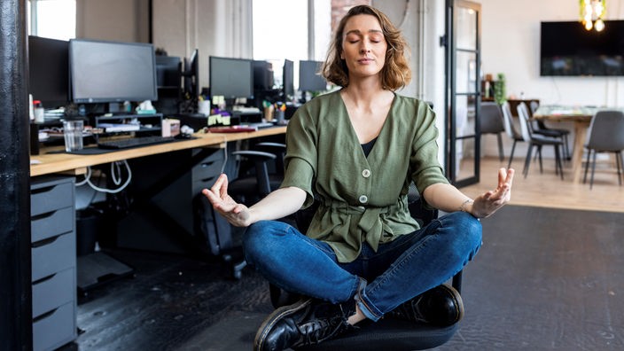 Eine Frau sitzt auf einen Bürostuhl in einem Büro und meditiert.