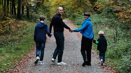 Eine Mann, eine Frau und zwei Kinder laufen auf einem Waldweg und halten sich an den Händen