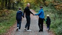 Eine Mann, eine Frau und zwei Kinder laufen auf einem Waldweg und halten sich an den Händen