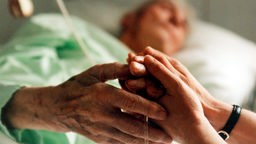 Symbolbild Pflege: Eine Krankenschwester hält die Hand einer sterbenskranken Patientin.