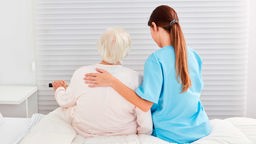 Eine junge Pflegerin hilft einer Seniorin aus dem Bett