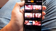 Ein Mann hält ein Smartphone in der Hand, auf dem Bildschirm sind Pornobilder
