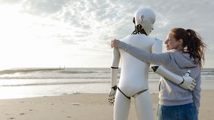 Ein Roboter und ein Frau stehen Arm in Arm am Strand