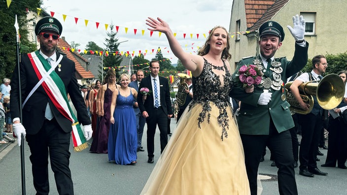 Der Schützenkönig und seine Frau schreiten in einem festlichen Umzug, gefolgt von der Schützern-Bruderschaft, durch eine Straße in Arnsberg-Herdringen.