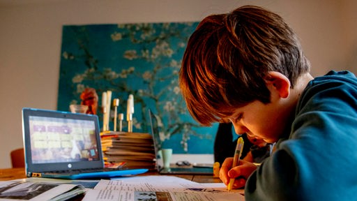 Symbolbild Lernrückstände durch Corona: Ein Junge sitzt zuhause am Tisch und macht alleine Hausaufgaben