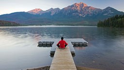 Ein Mann meditiert auf einem Steg vor einem Bergsee