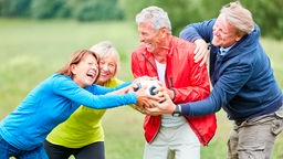 Gruppe Senioren hat Spaß beim Raufen und Spiel mit einem Fußball im Park