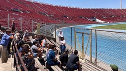 Eine Gruppe von Menschen sitzt im chilenischen Nationalstadion. Vor ihnen steht eine Frau, die etwas erklärt.