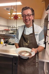 Sternekoch Elmar Simon steht in seiner Küche mit einem Teller Linsensuppe in der Hand