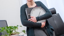 Eine Frau sitzt in einem Büro und hält eine Uhr in der Hand 