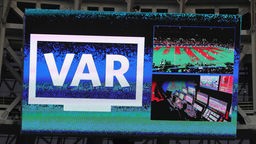 Auf der Anzeigetafel in einem Stadion ist der Schriftzug "VAR" für Video Assistent Referee zu sehen.