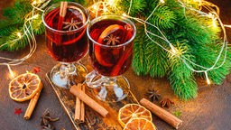 Zwei Gläser roter Weihnachtsbowle mit Zimtstangen vor Weihnachtsdekoration