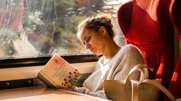 Eine Frau schläft in einem Zug mit einem Buch in der Hand
