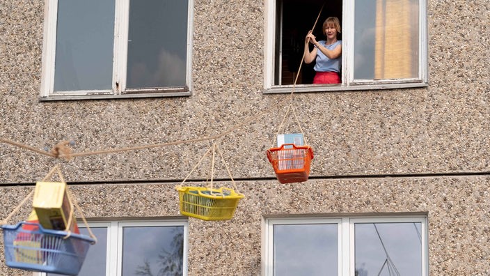 Szene aus dem Film "Zwei zu eins" (2024): Sandra Hüller steht als Maren in einem Fenster, von dem aus Wäschekörbe an einer Leine nach draußen gespannt sind-