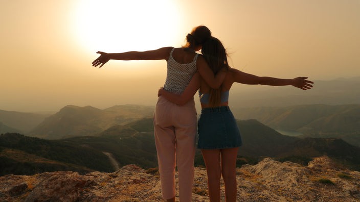 2 Frauen umarmen einander vor einem Sonnenuntergang