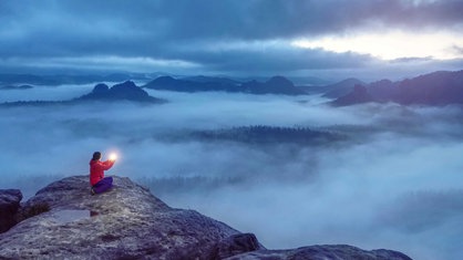 Sitzende Frau auf einer Bergspitze mit Licht in der Hand.