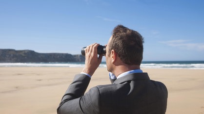 Ein Mann blickt mit einem Fernglas in die Ferne, während er am Strand steht