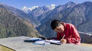 Ein Junge sitzt an einem Tisch in den Bergen und schreibt in ein Notizheft.