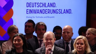 Olaf Scholz, Nancy Faeser und Reem Alabali-Radovan vor dem Hintergrund: Deutschland. Einwanderungsland.