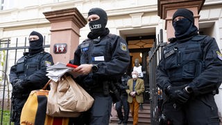 Bei einer Razzia gegen sogenannte «Reichsbürger» führen vermummte Polizisten, nach der Durchsuchung eines Hauses Heinrich XIII Prinz Reuß (hinten, Mitte) zu einem Polizeifahrzeug. Ein Polizist trägt dabei, Tüten, eine Tasche und Papiere. 