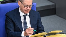 Bundeskanzler Olaf Scholz (SPD) sitzt in der Regierungsbank im Deutschen Bundestag und bearbeitet Akten. Dabei trägt er eine schwarze Brille.