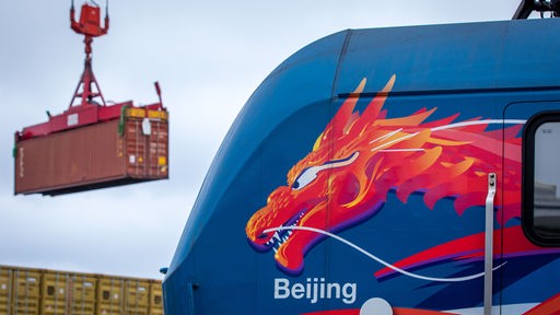 Ein Container wird hinter einer Lokomotive mit einem asiatischen Drachenkopf und dem Schriftzug "Beijing" nach der Ankunft eines ersten Schiffs einer neuen "Seidenstraßen"-Verbindung zwischen China und Deutschland im Hafen von Mukran entladen.