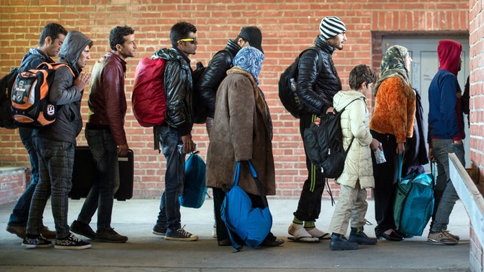 Flüchtlinge warten mit ihrem Gepäck auf ihre Weiterfahrt zur Unterkunft