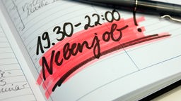 Ein Kugelschreiber liegt auf einem Kalender, in dem das Wort "Nebenjob" hervorgehoben ist.