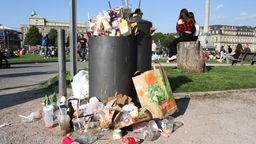 Plastikmüll liegt in, um und auf einem Mülleimer.