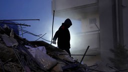 Ein Mann sucht in den Trümmern eines zerstörten Gebäudes nach Menschen.