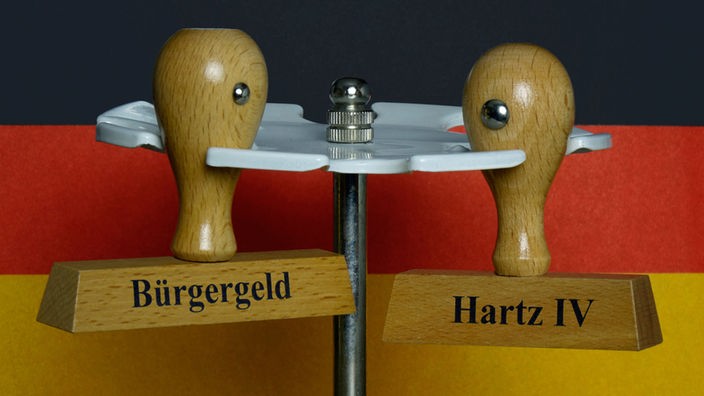 Stempel mit den Aufdrucken Bürgergeld und Hartz IV hängen vor einer Deutschlandfahne