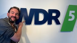 Philipp Scharrenberg posiert vor dem WDR5 Logo