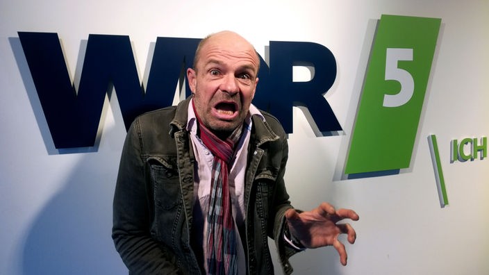 Kabarettist Thilo Seibel posiert in Golum-Pose vor dem WDR-5-Logo