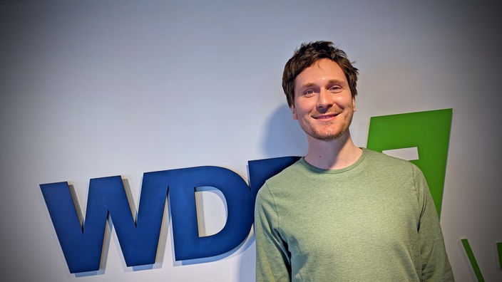 Hosea Ratschiller posiert vorm WDR5 Logo