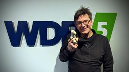 Martin Kaysh posiert mit kleinem Stoffadler vorm WDR 5 Logo