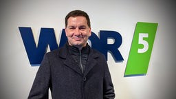Moritz Netenjakob posiert im Wintermantel vor dem WDR-5-Logo
