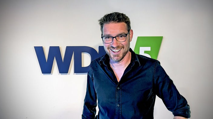 Sascha Thamm posiert vor dem WDR5 Logo