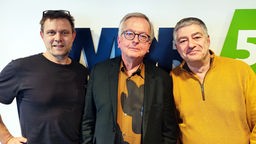 Satiriker Hans Zippert steht zwischen den Moderatoren Henning Bornemann und Axel Naumer im WDR 5-Studio und lächelt