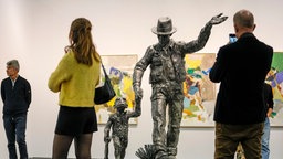 Besucher schauen sich das Kunstwerk "Beuys mit Affe" von Jörg Immendorf auf der Art Cologne 2024 an.