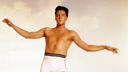 Filmszene aus "Paradise Hawaiian Style": Elvis Presley mit ausgebreiteten Armen und in Badehose.