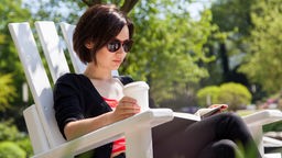 Eine junge Frau sitzt in einem Park und liest ein Buch. 