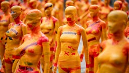 Die Installation besteht aus 222 orangefarbenen Schaufensterfiguren, die mit Klebebändern und Statements eingewickelt sind.