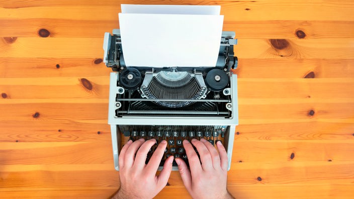 Hände auf einer alten Schreibmaschine mit eingezogenem Blatt Papier